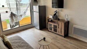 Une chambre avec un lit, une petite table, une télévision, un réfrigérateur et une fenêtre avec un rideau.
