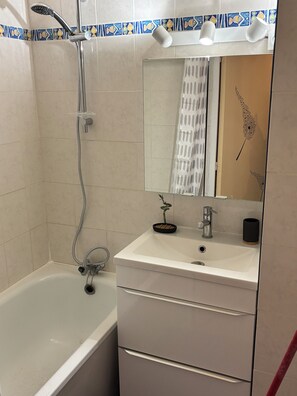 A bathroom with a bathtub, a sink, a mirror, and a showerhead. - Bright village apartment with terrace and parking 50m from the sea (Le Barcarès)