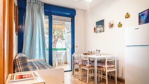 Ein gemütlicher Raum mit einem Bett, einem Esstisch mit Stühlen, einem weißen Kühlschrank und einem Fenster mit blauen Vorhängen.