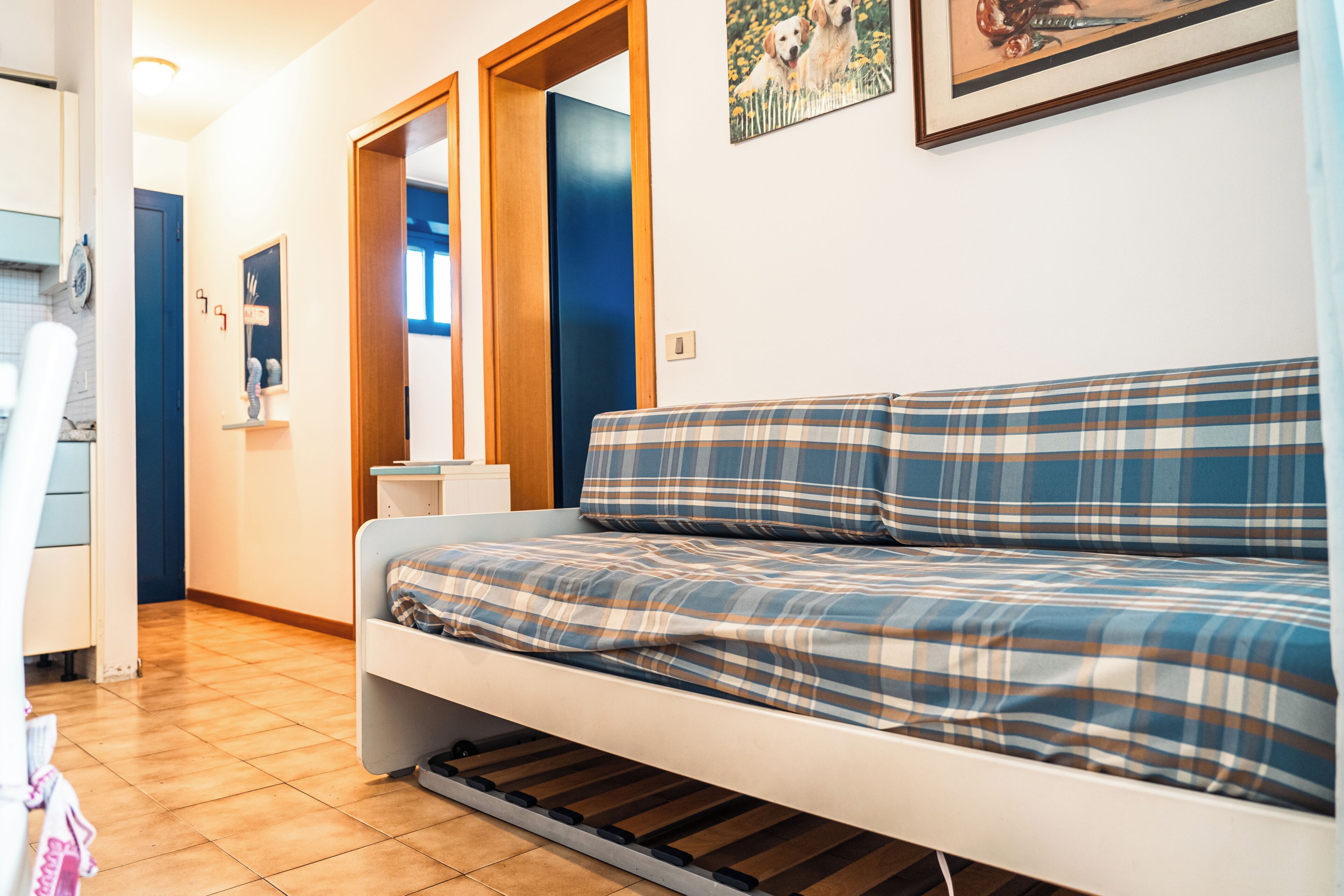 Ein kleiner, gemütlicher Raum mit einem Bett, einer Holztür und einem gerahmten Bild an der Wand.
