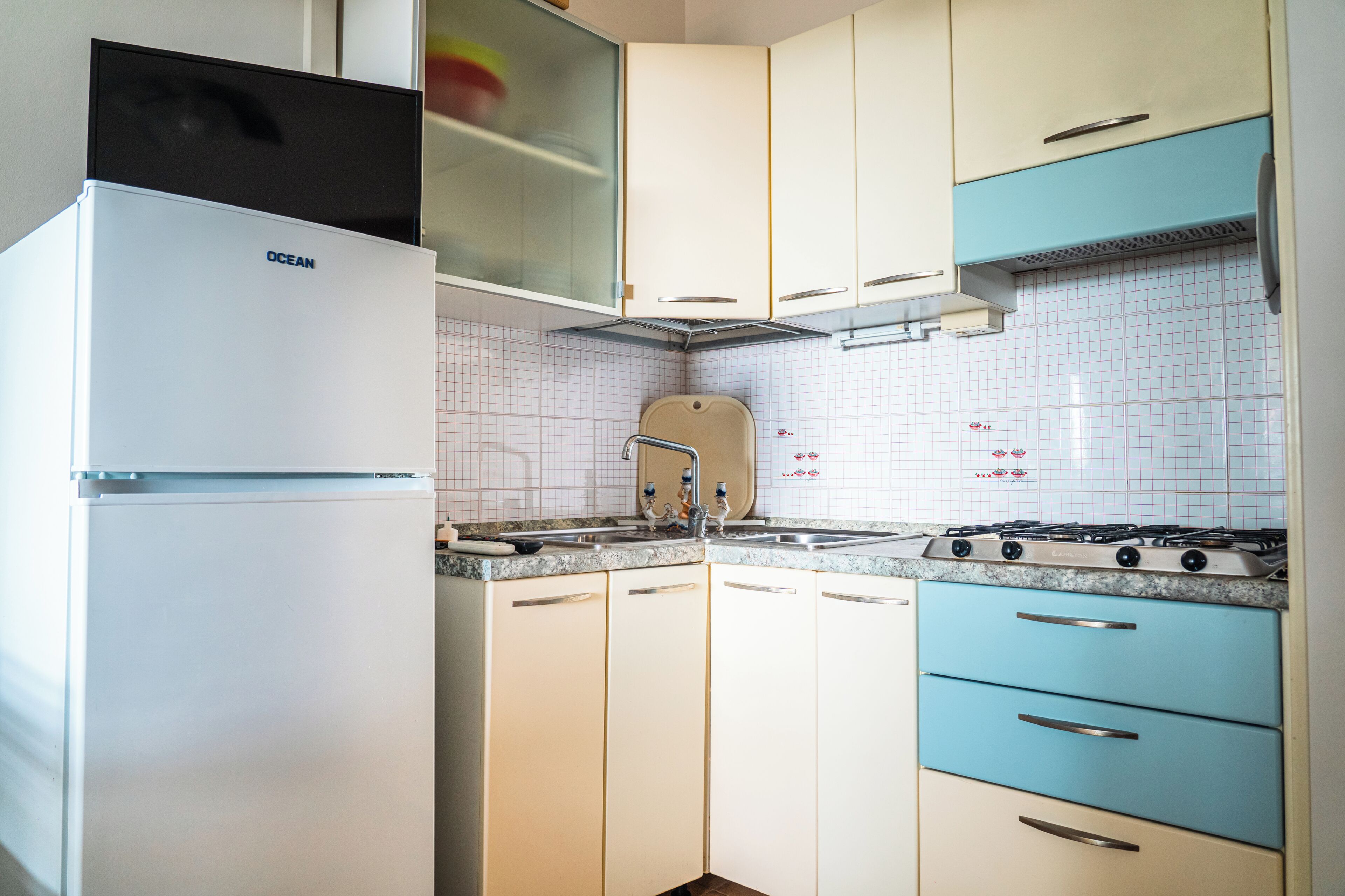 A kitchen with white and blue cabinets, a stove, and a refrigerator.