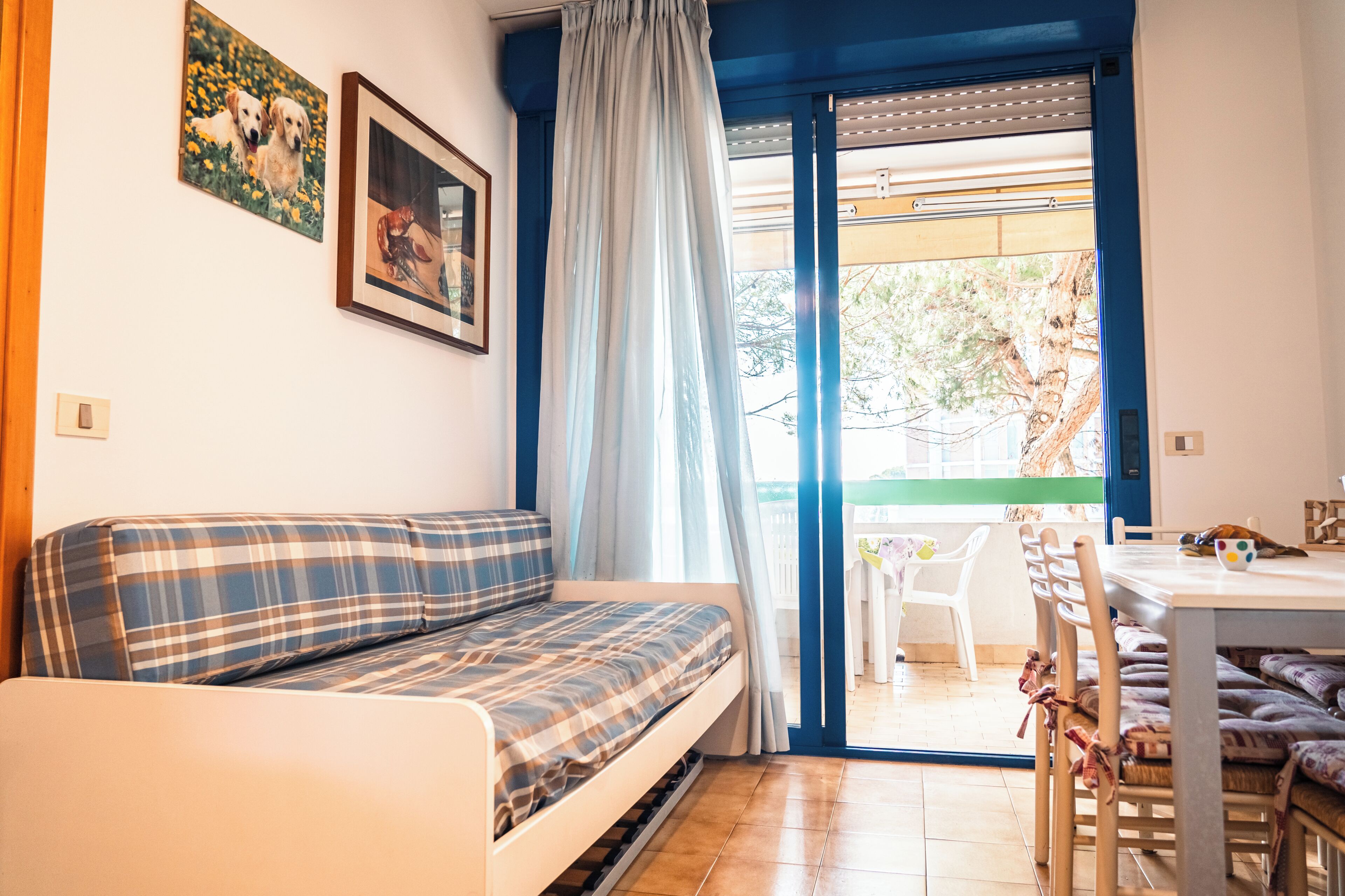 A cozy room with a sofa, a dining table, and chairs. There is a window with curtains, and a painting on the wall.