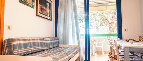A cozy room with a sofa, a dining table, and chairs. There is a window with curtains, and a painting on the wall.