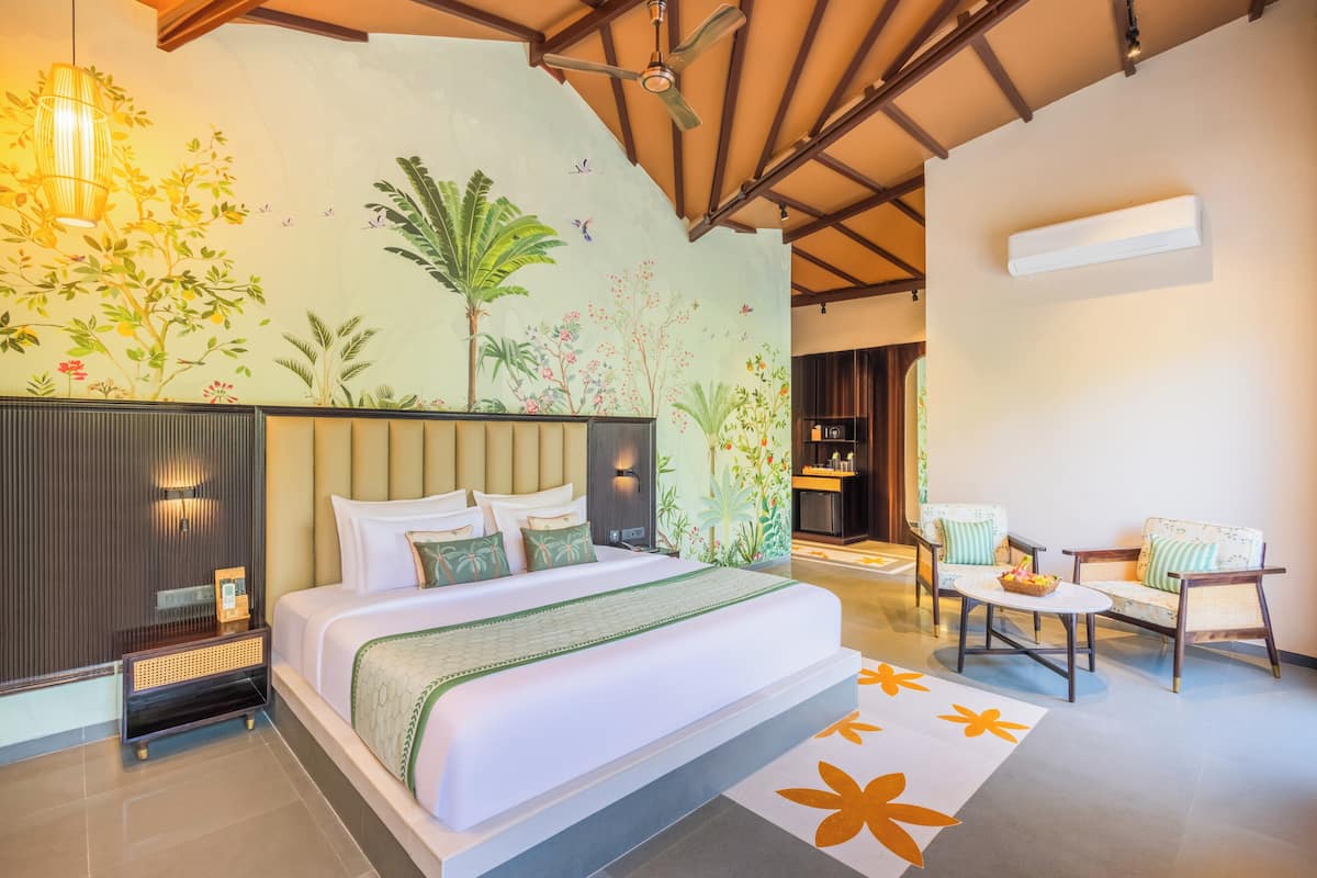 Ein modernes Hotelzimmer mit einem großen Bett, einer Sitzecke mit zwei Sesseln, einer Wandmalerei und einem Deckenventilator.
