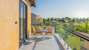 Ein Balkon mit zwei Korbstühlen und einem kleinen Tisch, mit Blick auf eine grüne Landschaft und angrenzende Häuser.