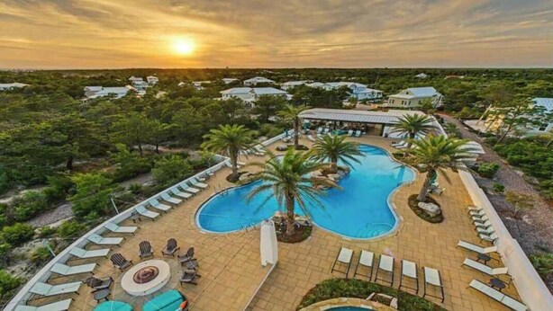 Ein Resort mit großem Schwimmbecken, Liegestühlen und Palmen.