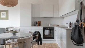 A modern kitchen with white cabinets, a round dining table, and a hanging coat rack. - Clover House 1BR by Daniel&Jacob's (København)