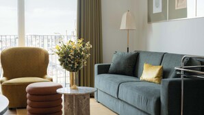 A modern living room with a grey sofa, a mustard-colored armchair, and a round coffee table with a vase of flowers. - Clover House 1BR by Daniel&Jacob's (København)