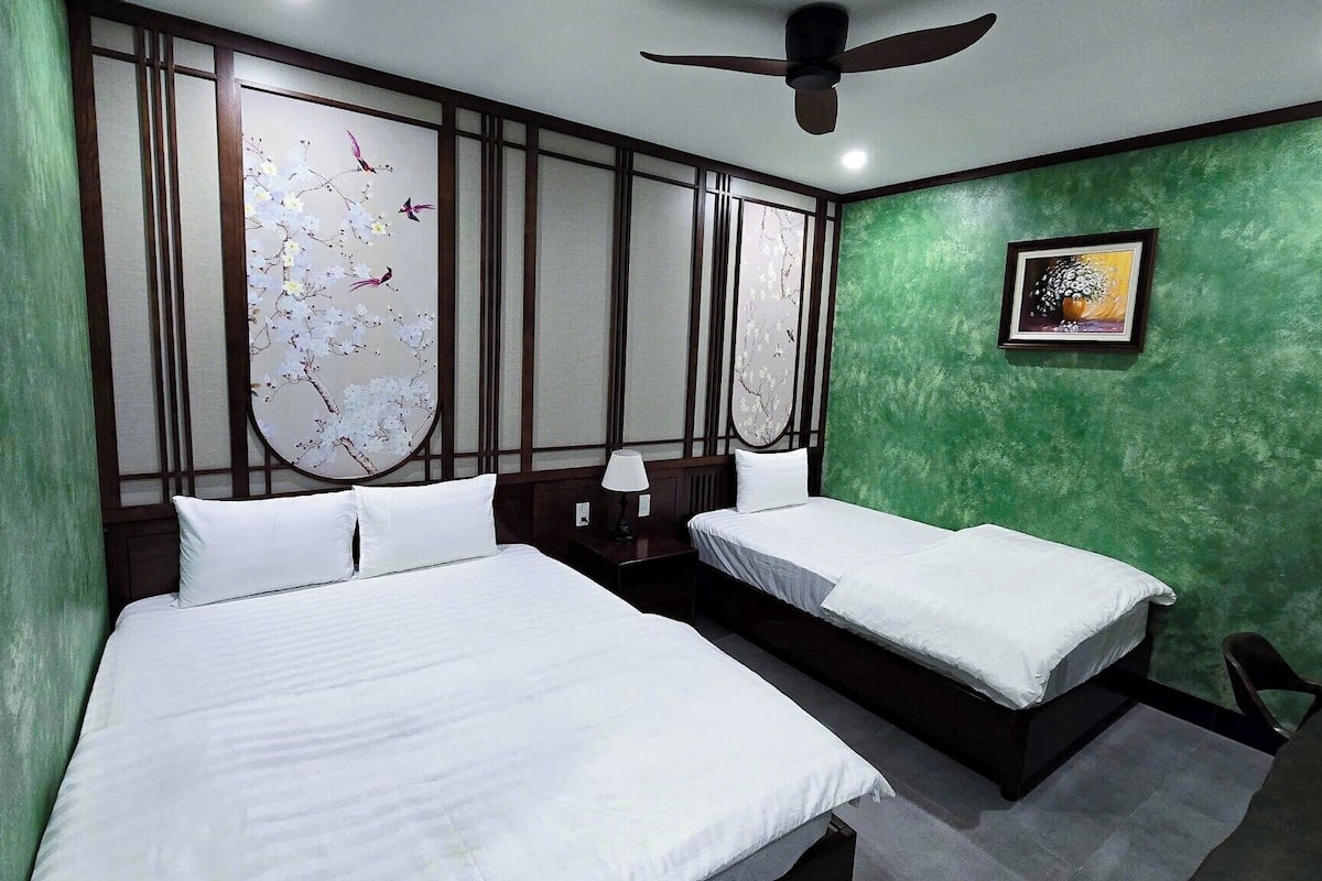 A hotel room with two beds, a ceiling fan, a green wall, and a framed artwork.
