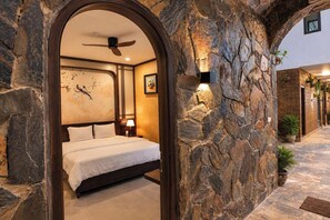 A bedroom with a stone archway, a bed, a ceiling fan, and a nightstand with a lamp. - Serena Tam Coc Hotel  (Nam Hoa Lu)