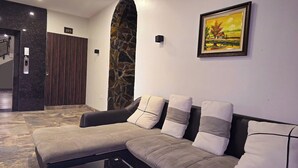 A modern lobby with a reception desk, a stone wall, a sofa with cushions, and a framed painting on the wall. - Serena Tam Coc Hotel & Villa (Nam Hoa Lu)