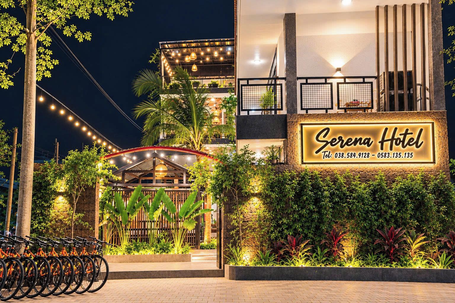 Entrada de hotel con un letrero, una zona cubierta con iluminación y un espacio para estacionar bicicletas.