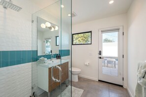 Un baño moderno con cabina de ducha de vidrio, un lavabo blanco sobre mueble de madera y un inodoro.