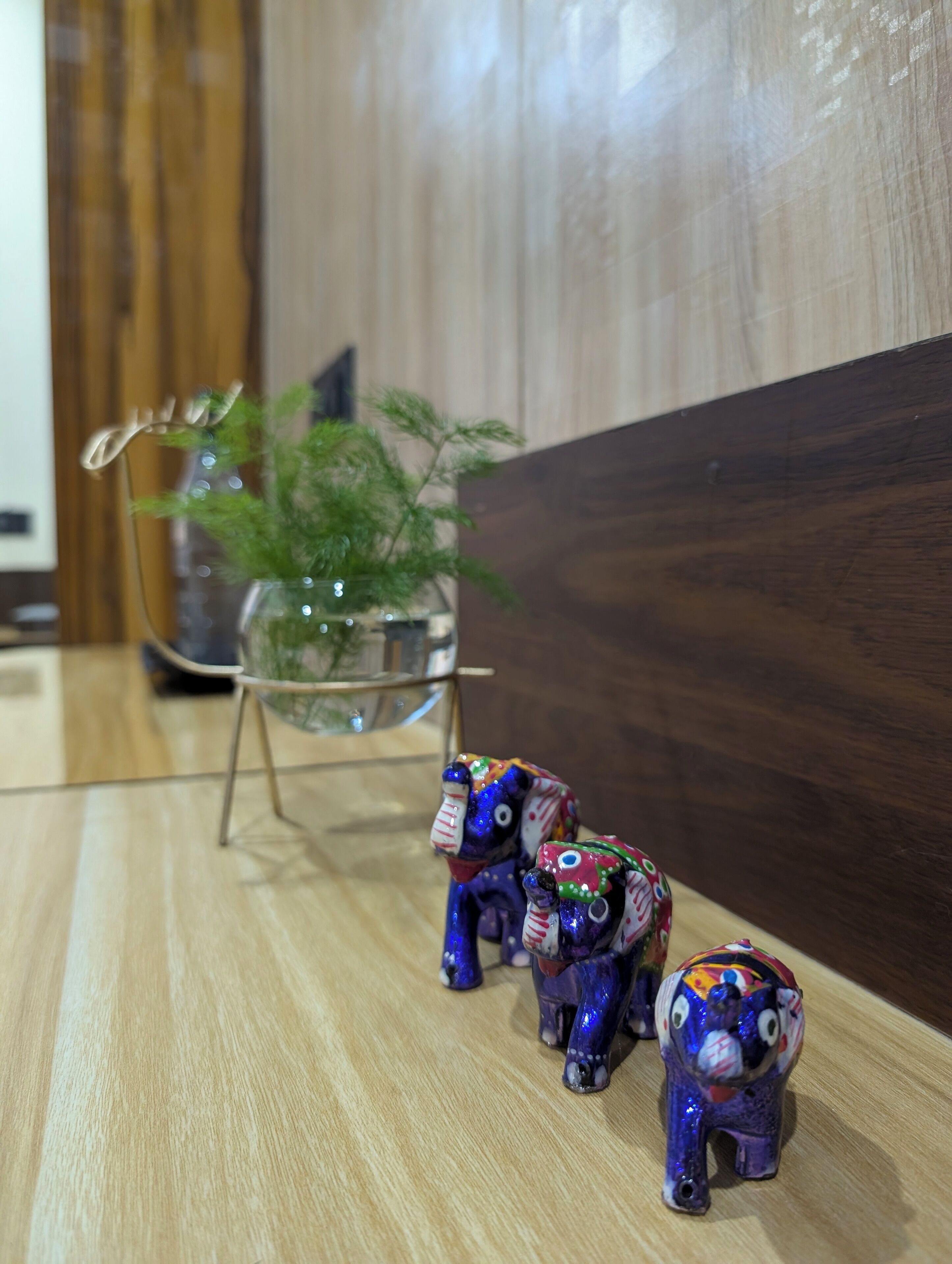 Un pavimento in legno con un tavolo in vetro che ospita una pianta e due figurine di elefanti colorati.