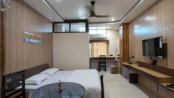 A modern hotel room with a bed, a round table with chairs, a TV, and a desk with a chair.
