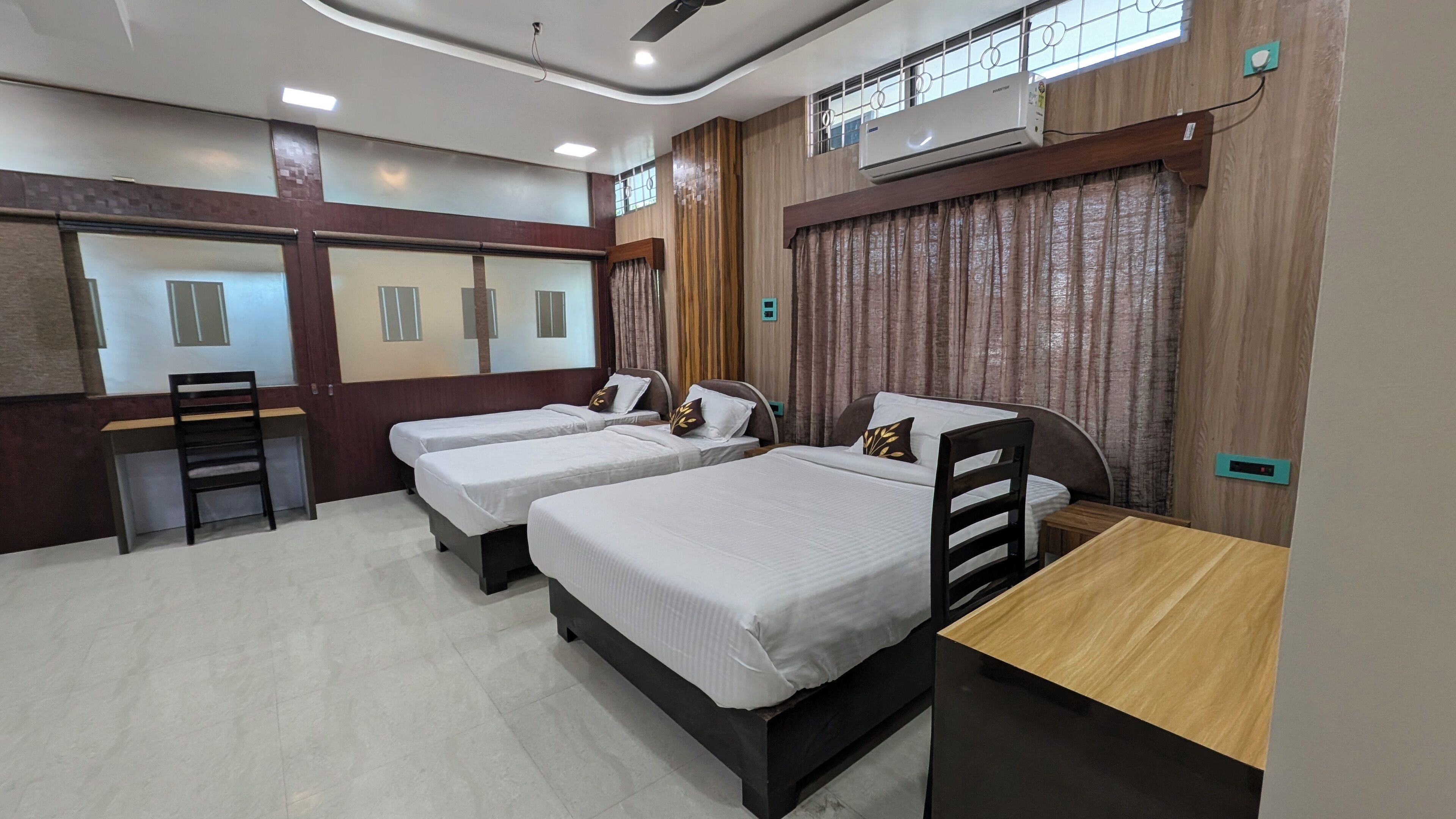 A hotel room with three single beds, a desk, a chair, and an air conditioning unit.