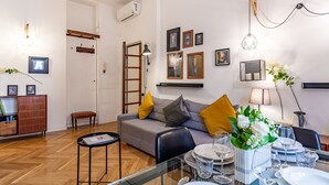 Ein modernes Wohnzimmer mit Sofa, Esstisch und verschiedenen Wandleuchten.