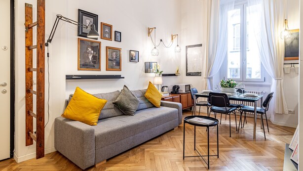 Ein modernes Wohnzimmer mit grauem Sofa, Holzboden und einem Essbereich mit Tisch und Stühlen.