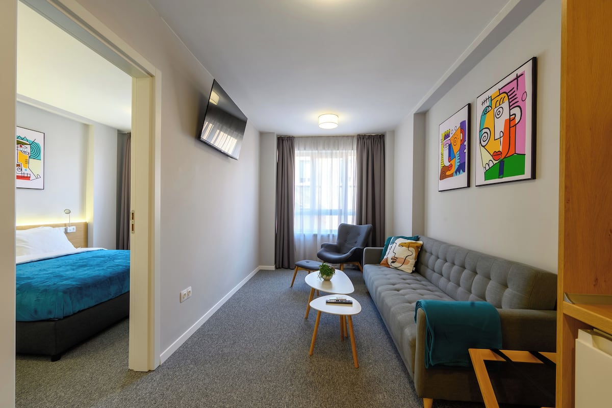 Una habitación de hotel moderna con cama, sofá, mesa de centro y televisor montado en la pared.