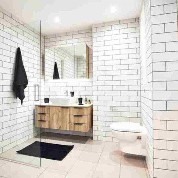 Une salle de bain moderne avec des carreaux de métro blancs, un meuble-lavabo en bois, une serviette noire et une cabine de douche en verre.