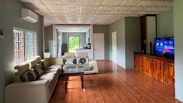 Un amplio salón con piso de madera, un sofá modular, una mesa de centro y un televisor sobre un mueble de madera.