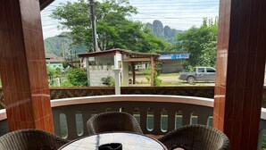 Un balcón con sillas de mimbre y una mesa de vidrio, con vistas a un paisaje verde y montañas distantes.