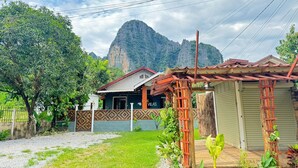 Una casa con techo rojo, una pérgola de madera y un jardín con diversas plantas.