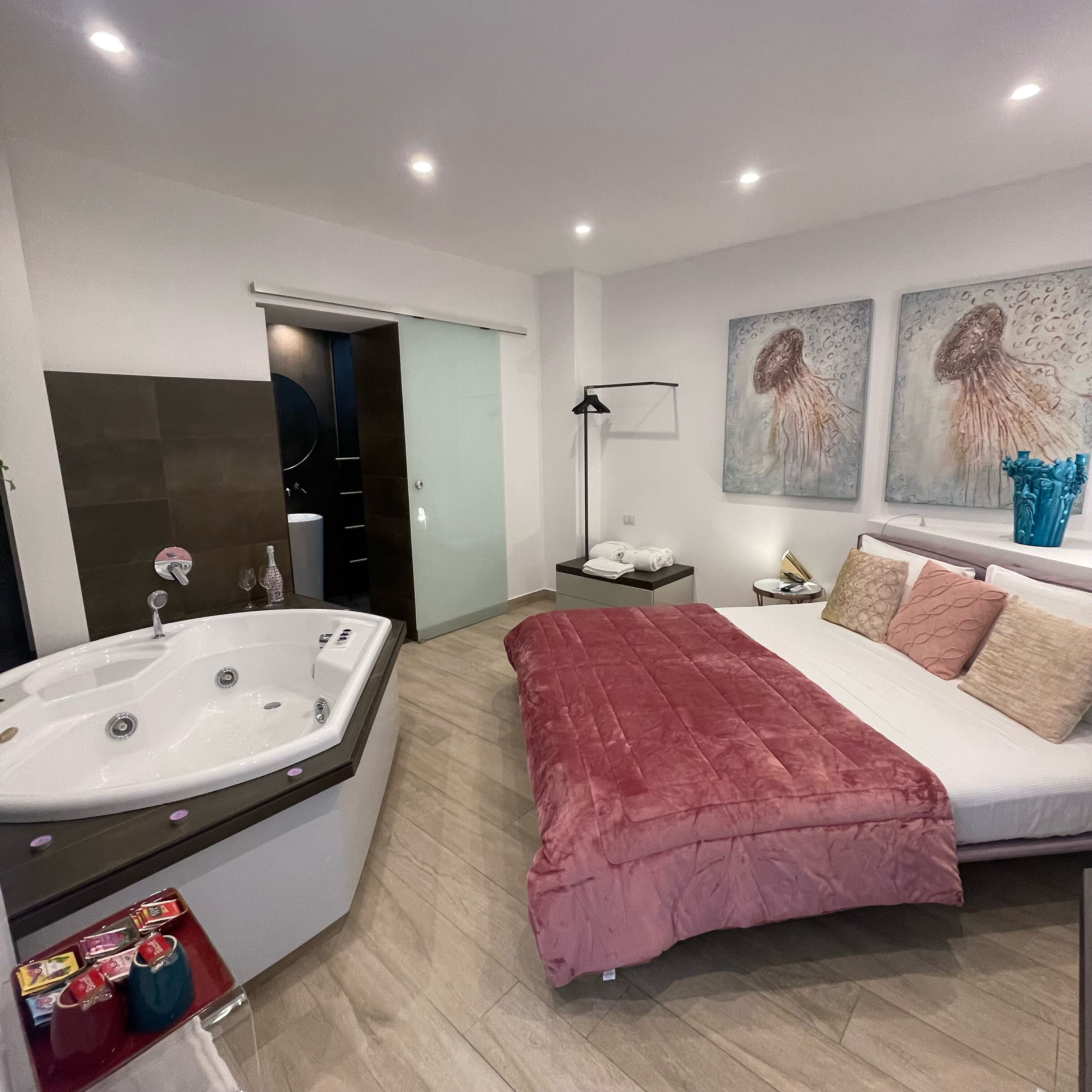 A modern bedroom with a large bed, a bathroom with a bathtub, and artwork on the wall.