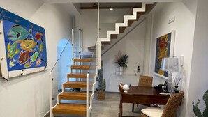 Ein modernes Interieur mit einer Holztreppe, einem Essbereich mit Korbstühlen und Kunstwerken an den Wänden.