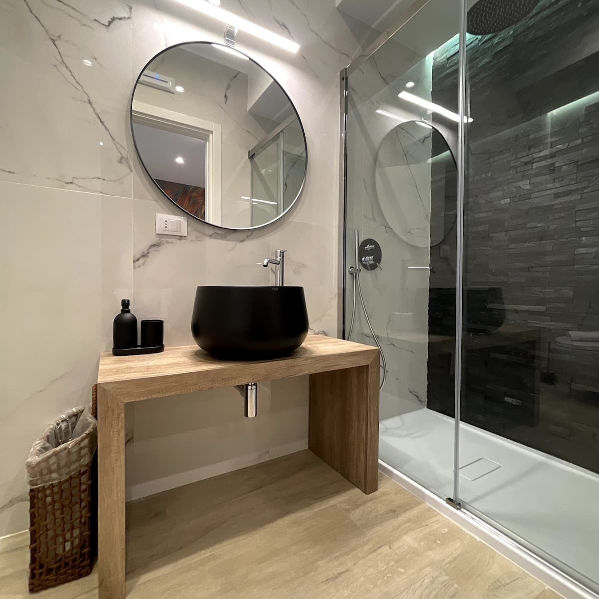 A modern bathroom with a wooden vanity, a black vessel sink, and a glass shower enclosure.