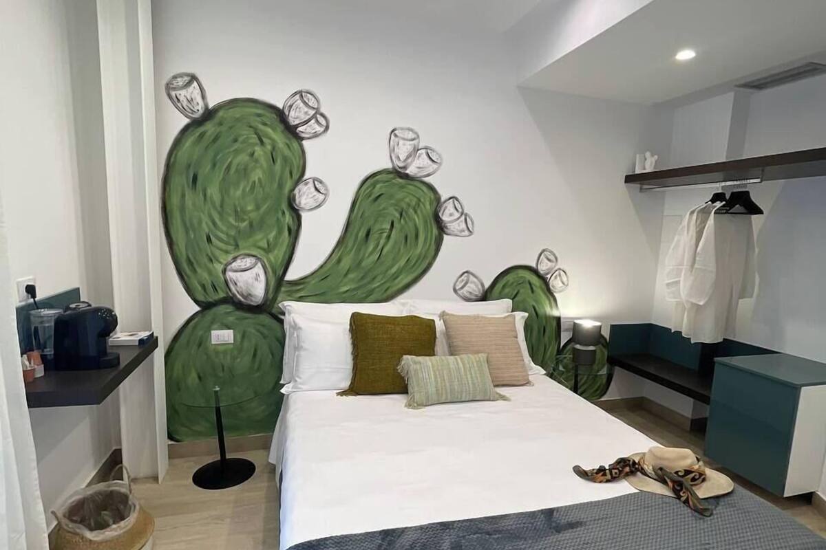 Une chambre moderne avec un grand lit, un mur décoré d’une fresque verte, une table de chevet et une armoire.