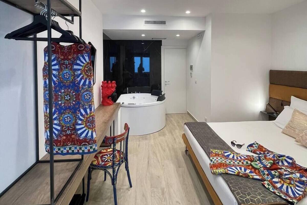 Une chambre d’hôtel moderne, équipée d’un lit, d’un bureau, d’une chaise et d’une salle de bain visible à travers une porte ouverte.