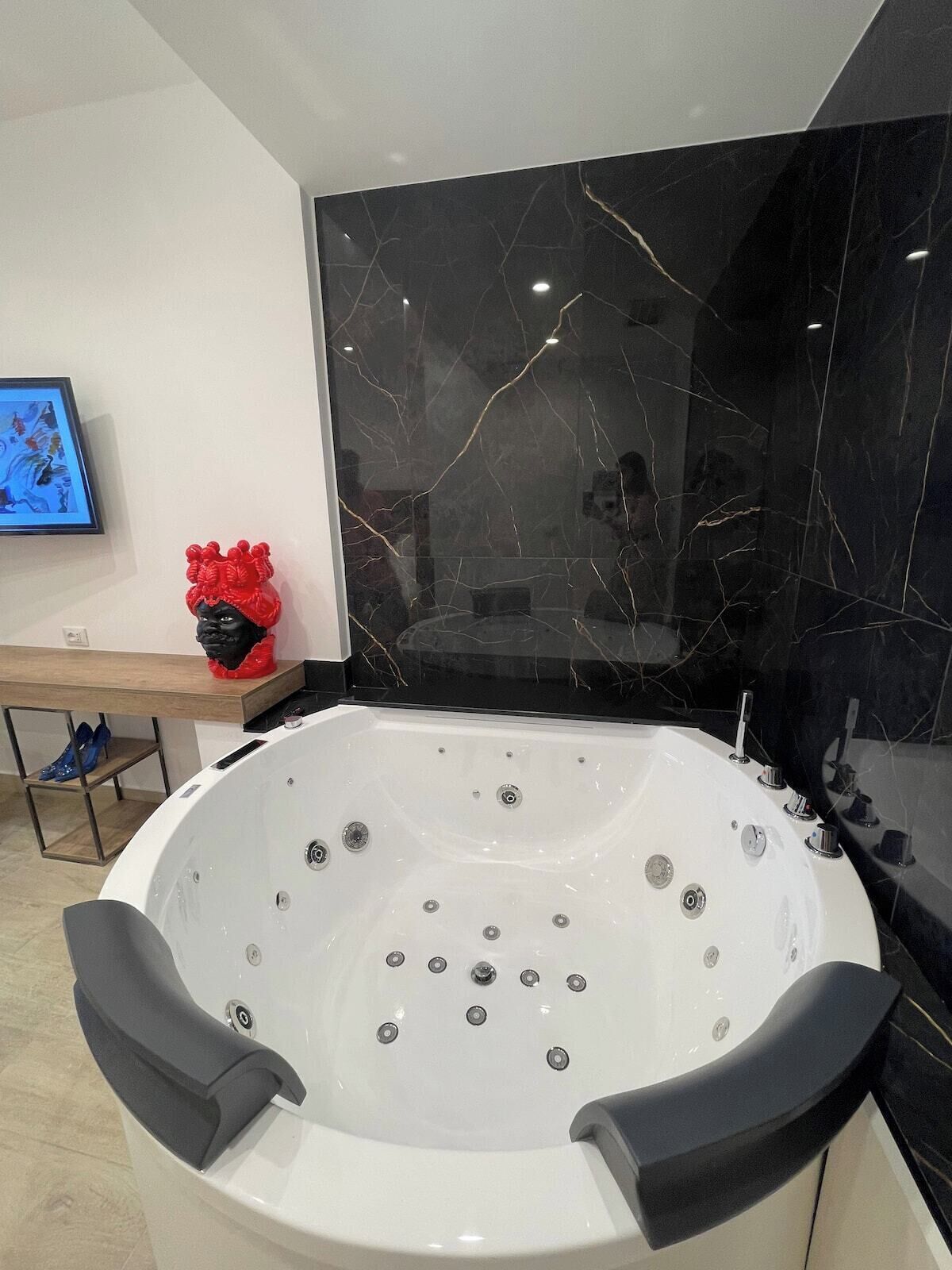 Een moderne badkamer met een groot, wit bad, zwarte marmeren wanden en een houten wastafelmeubel.