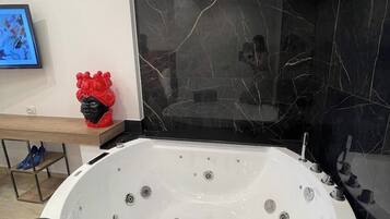 Een moderne badkamer met een groot, wit bad, zwarte marmeren wanden en een houten wastafelmeubel.