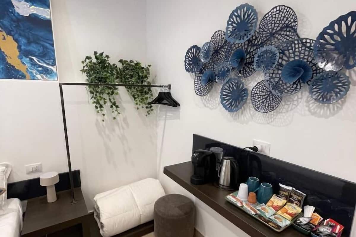Une salle de bain moderne agrémentée d’un grand tableau abstrait, d’un élément décoratif bleu mural, d’un porte-serviettes avec des plantes vertes, d’un coin café et d’une petite poubelle.