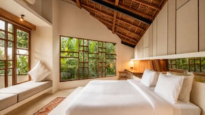 A bedroom with a large bed, a desk, a window with a view of greenery, and a sloped ceiling. - Designer 2-BR Villa Pool, 800m to Canggu Beach (Kecamatan Mengwi)