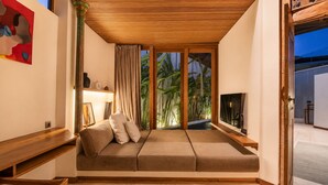 A room with a sofa, a TV, and a view of greenery outside. - Serene 1BR Villa 800 to Echo Beach, with Pool (Kecamatan Mengwi)