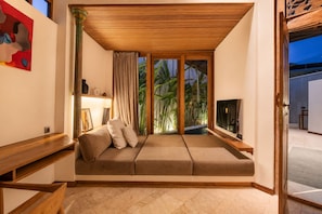 A cozy room with a sofa, a TV, and a view of greenery outside. - Serene 1BR Villa 800 to Echo Beach, with Pool (Kecamatan Mengwi)