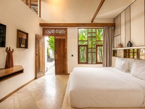 Un dormitorio con una cama grande, una puerta de madera, un ventanal con vistas a la vegetación y una estantería con objetos decorativos.