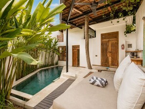 Un área junto a la piscina con terraza de madera, un sofá blanco con cojines y una mesita.