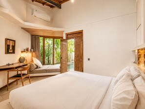 Ein Schlafzimmer mit einem Bett, einem Schreibtisch, einem Stuhl und Blick ins Grüne durch ein Fenster.