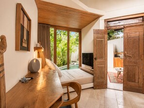 A room with a wooden table, a sofa, a TV, and a large window with a view of greenery. - Lush 1-BR Villa with Pool, 4 Mins to Echo Beach, (Kecamatan Mengwi)