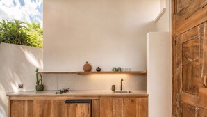 A compact kitchen with wooden cabinets, a countertop, a sink, and a shelf with kitchenware. - Opulent 1-BR Villa Just 800m from Canggu Beach (Kecamatan Mengwi)