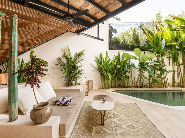 Un espace de vie extérieur moderne comprenant une piscine, un canapé, une table basse et diverses plantes.