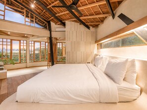 A bedroom with a large bed, wooden ceiling beams, and a view through a window.