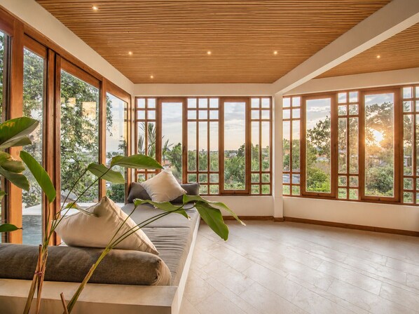 A spacious room with large windows, a wooden ceiling, and a sofa with cushions.