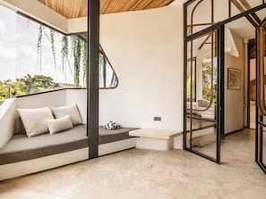 Un intérieur moderne avec un banc intégré, une porte vitrée donnant sur une autre pièce et une vue sur la verdure à l’extérieur.