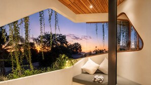Ein moderner Balkon mit gewölbter Glasscheibe, einer gepolsterten Sitzecke und Blick auf eine Sonnenlandschaft.