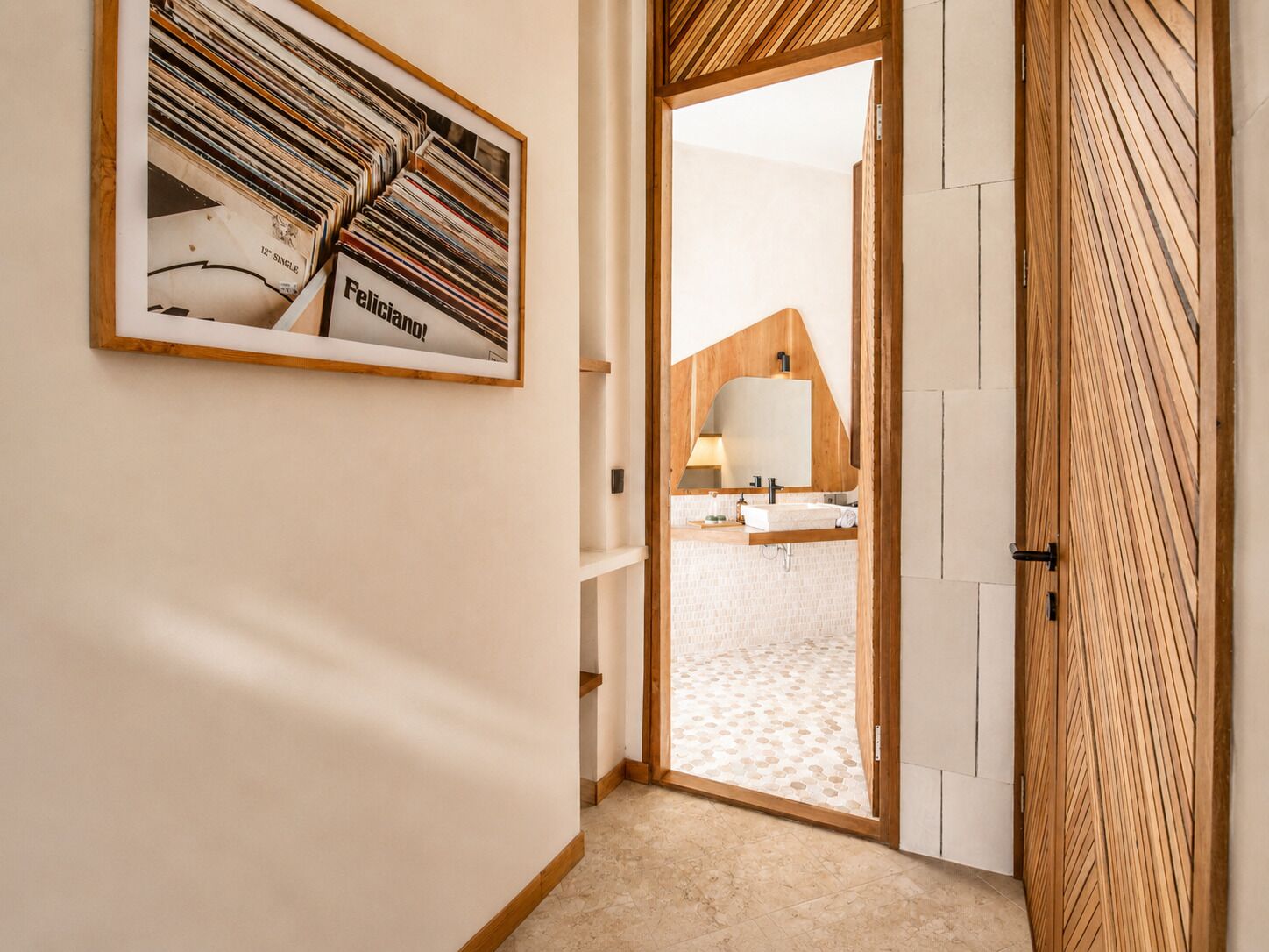 A hallway with a framed picture, a wooden door, and a glimpse of a bathroom with a sink and mirror.