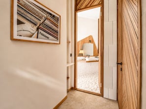 Un couloir avec un tableau encadré, une porte en bois et, au fond, on aperçoit une salle de bain avec un lavabo et un miroir.